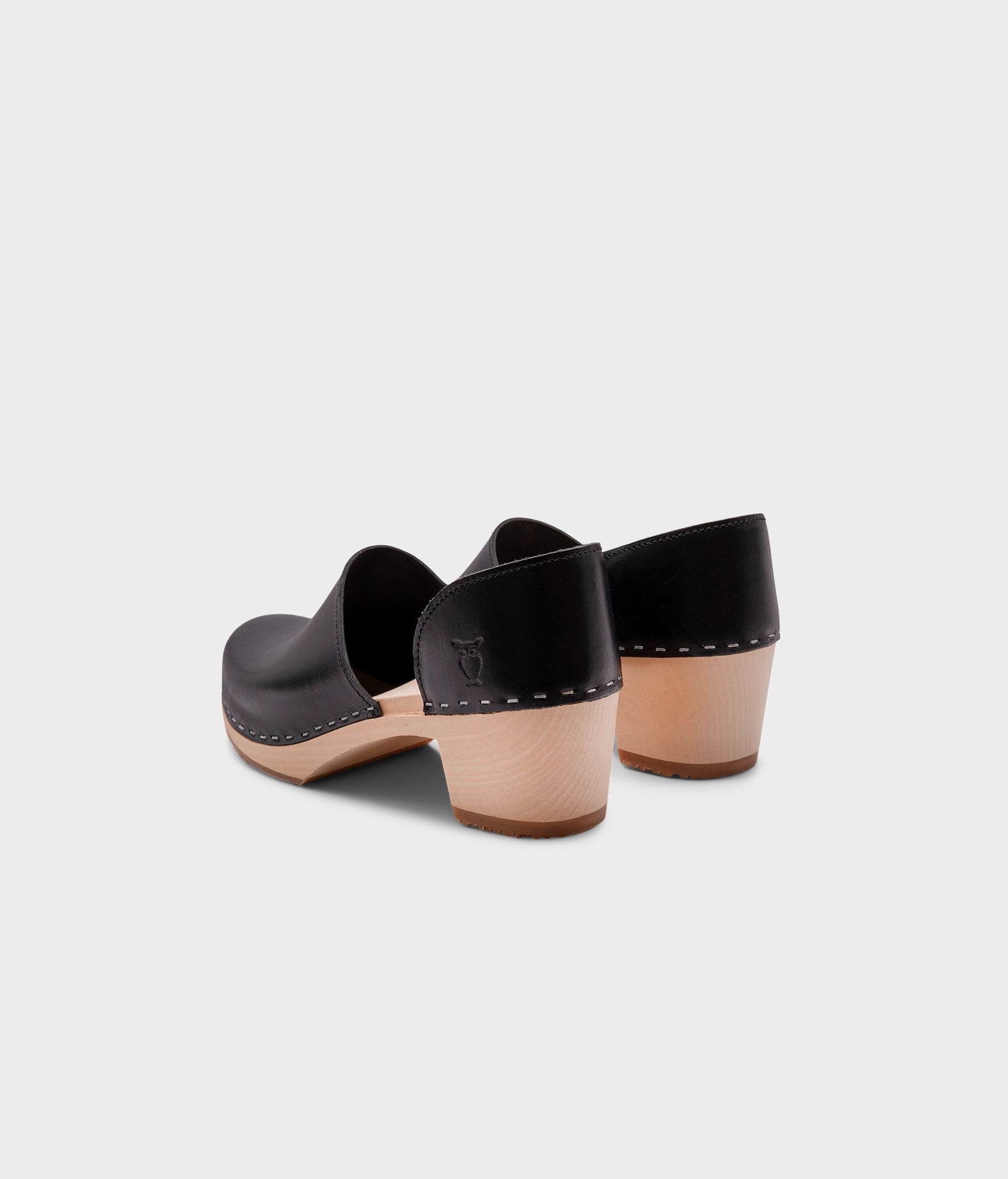 high heeled closed-back clogs in black vegetable tanned leather stapled on a light wooden base