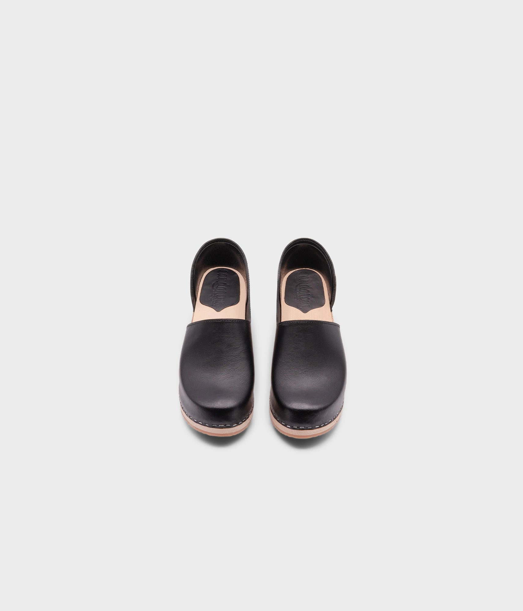 high heeled closed-back clogs in black vegetable tanned leather stapled on a light wooden base
