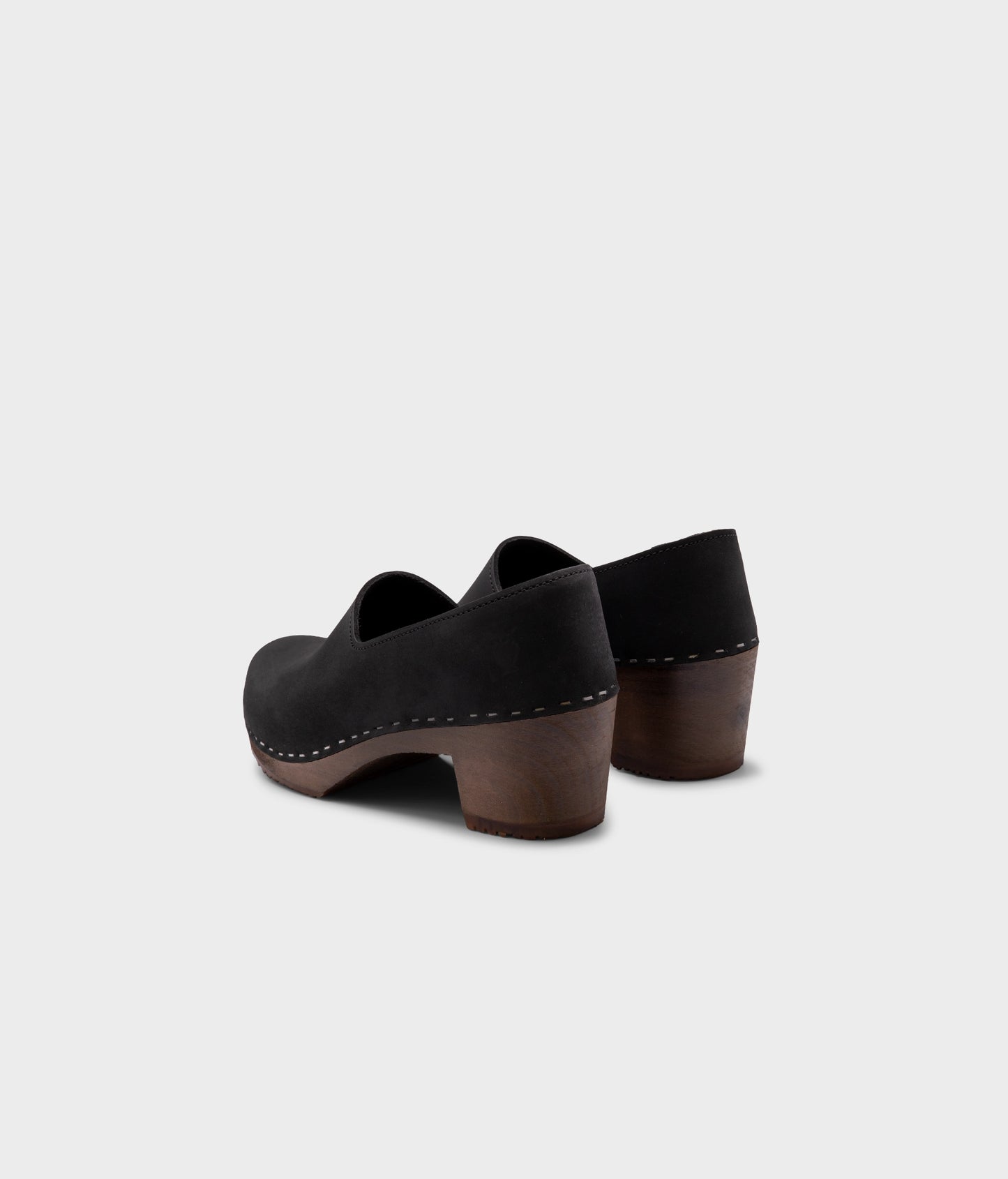 high heeled closed-back clogs in black nubuck leather stapled on a dark wooden base