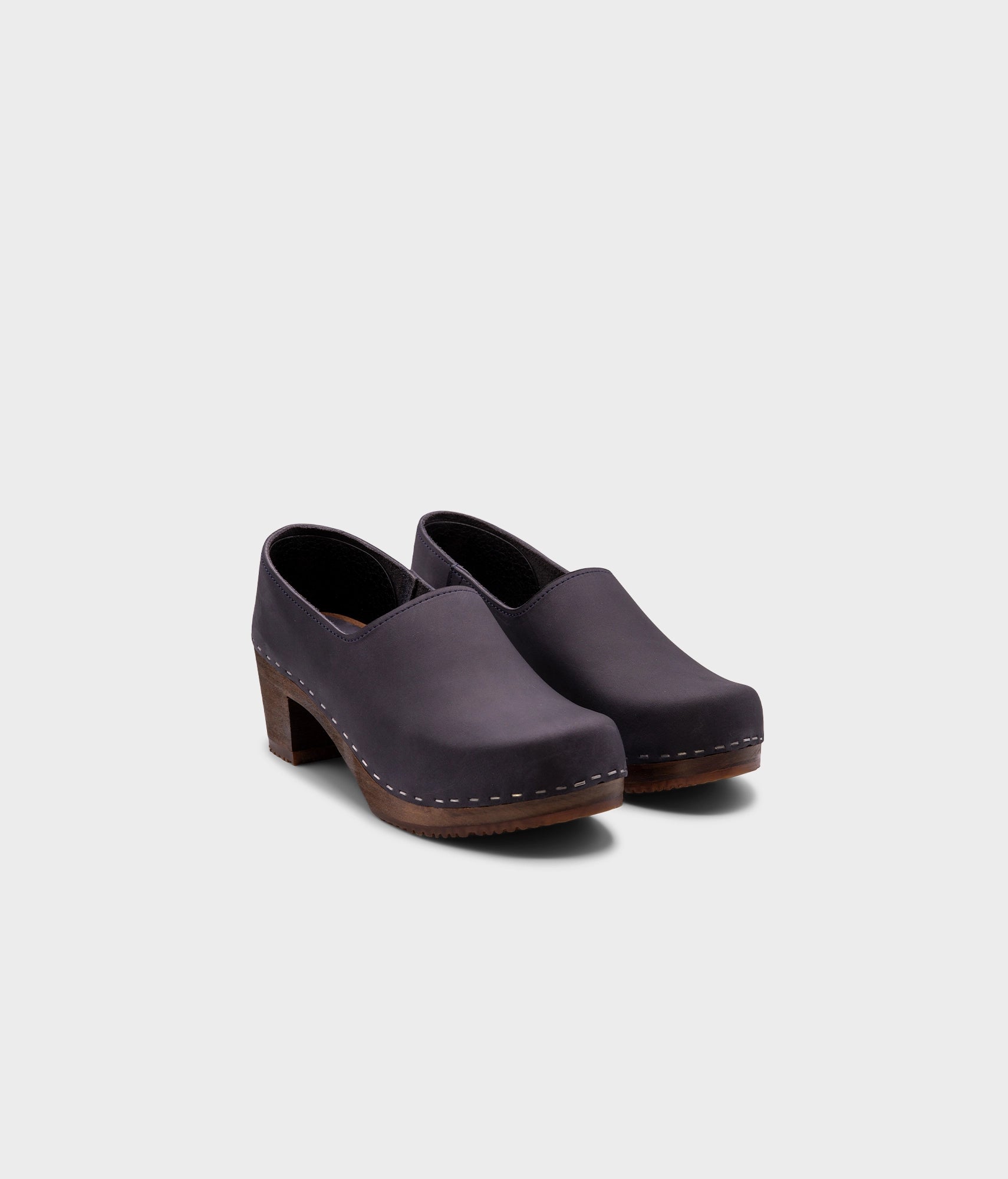 high heeled closed-back clogs in navy blue nubuck leather stapled on a dark wooden base