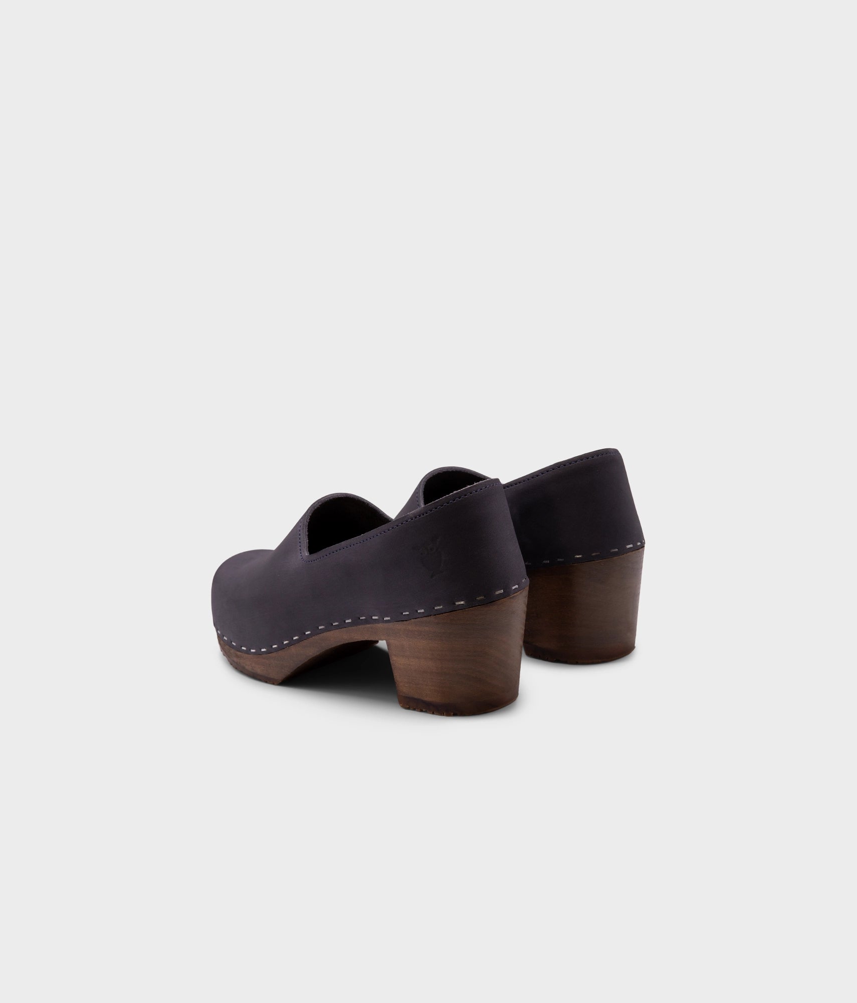 high heeled closed-back clogs in navy blue nubuck leather stapled on a dark wooden base