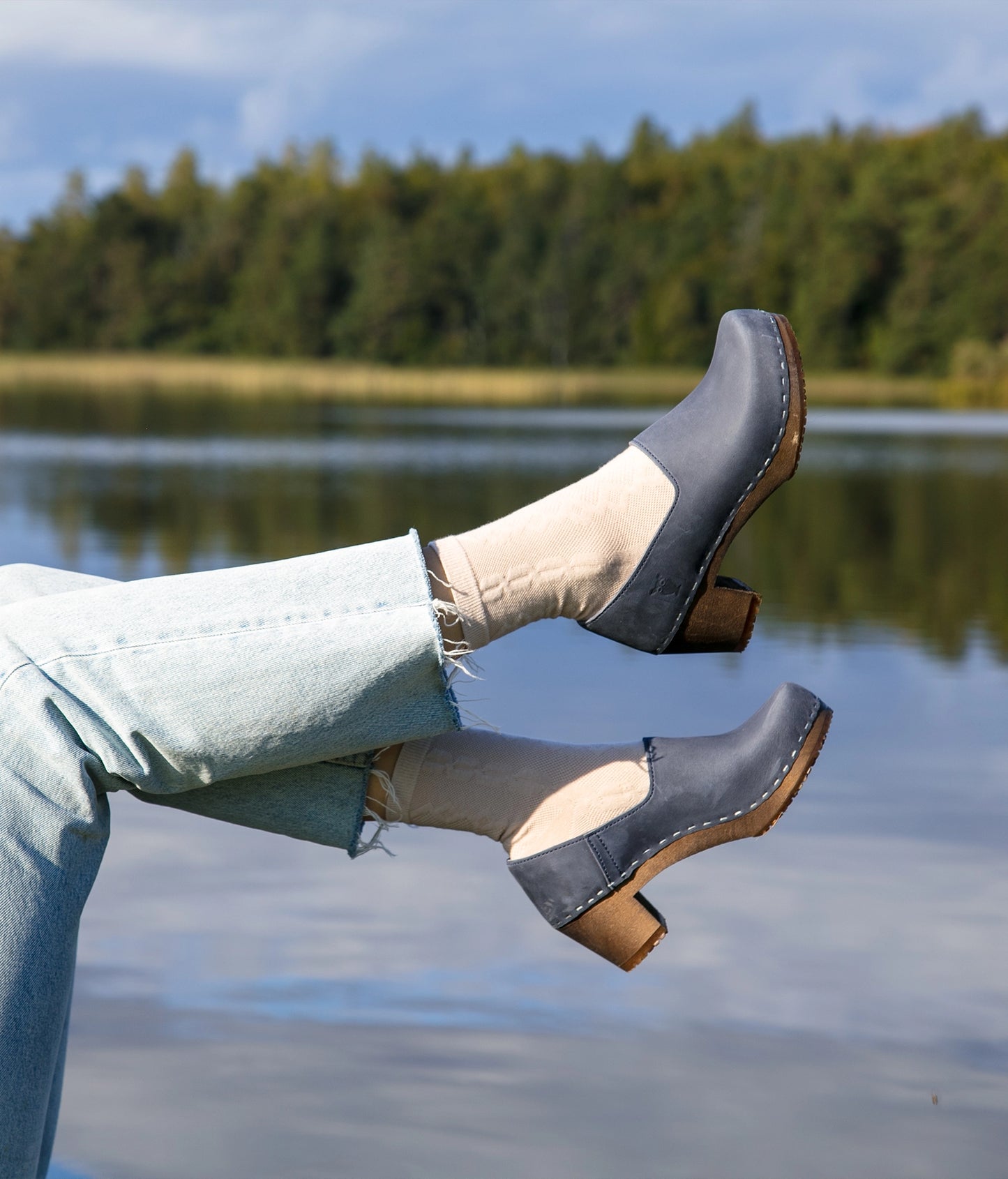 high heeled closed-back clogs in navy blue nubuck leather stapled on a dark wooden base