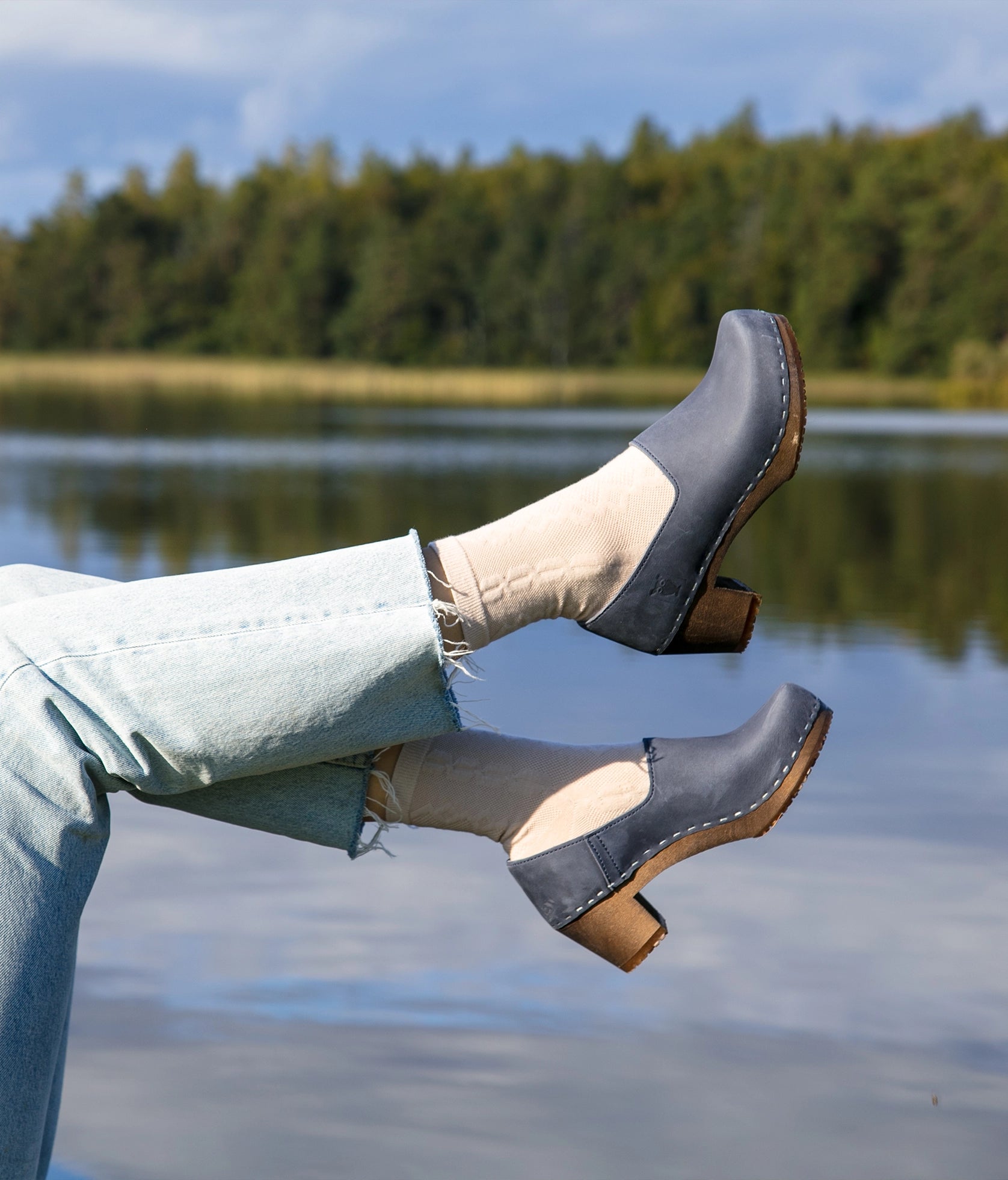 high heeled closed-back clogs in navy blue nubuck leather stapled on a dark wooden base