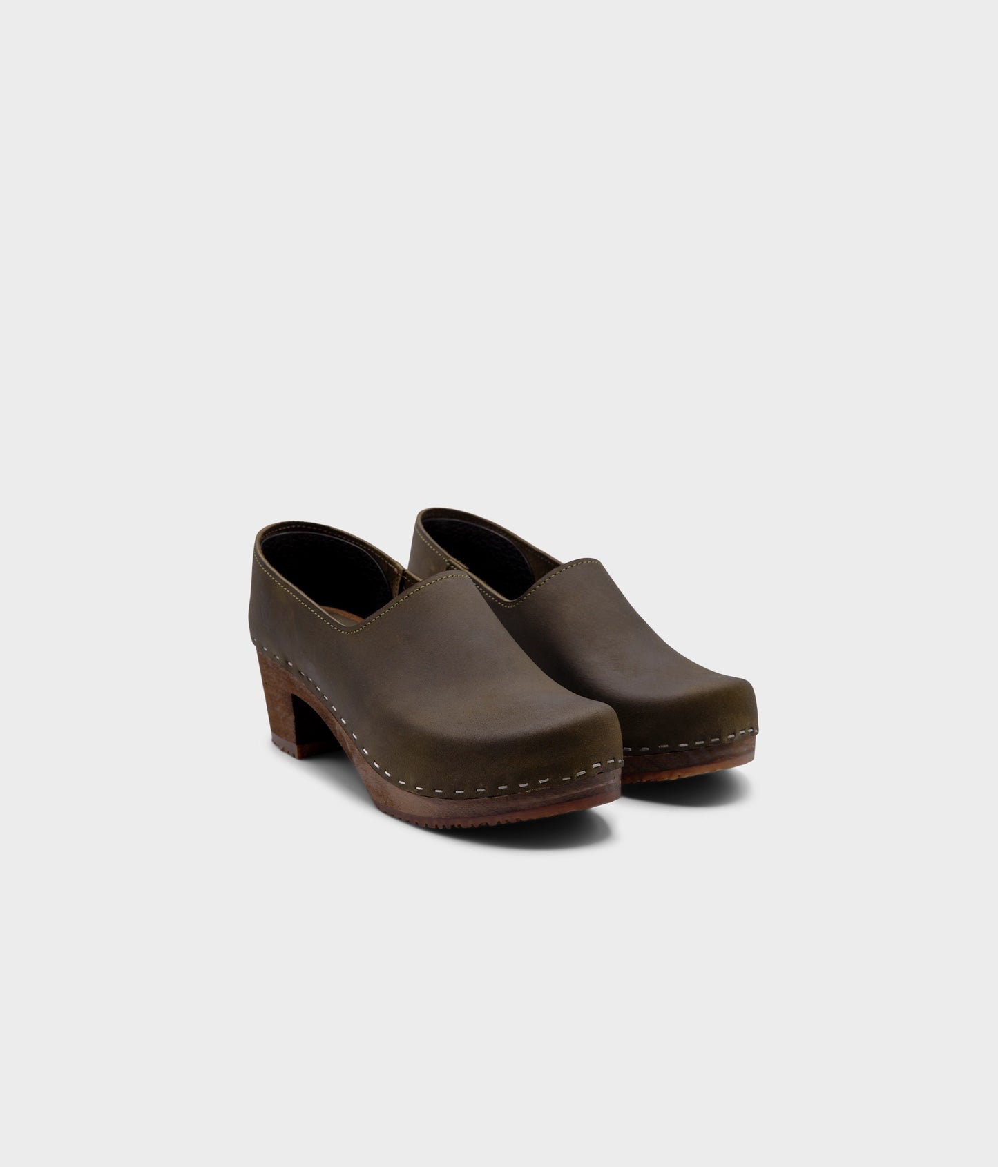 high heeled closed-back clogs in olive green nubuck leather stapled on a dark wooden base