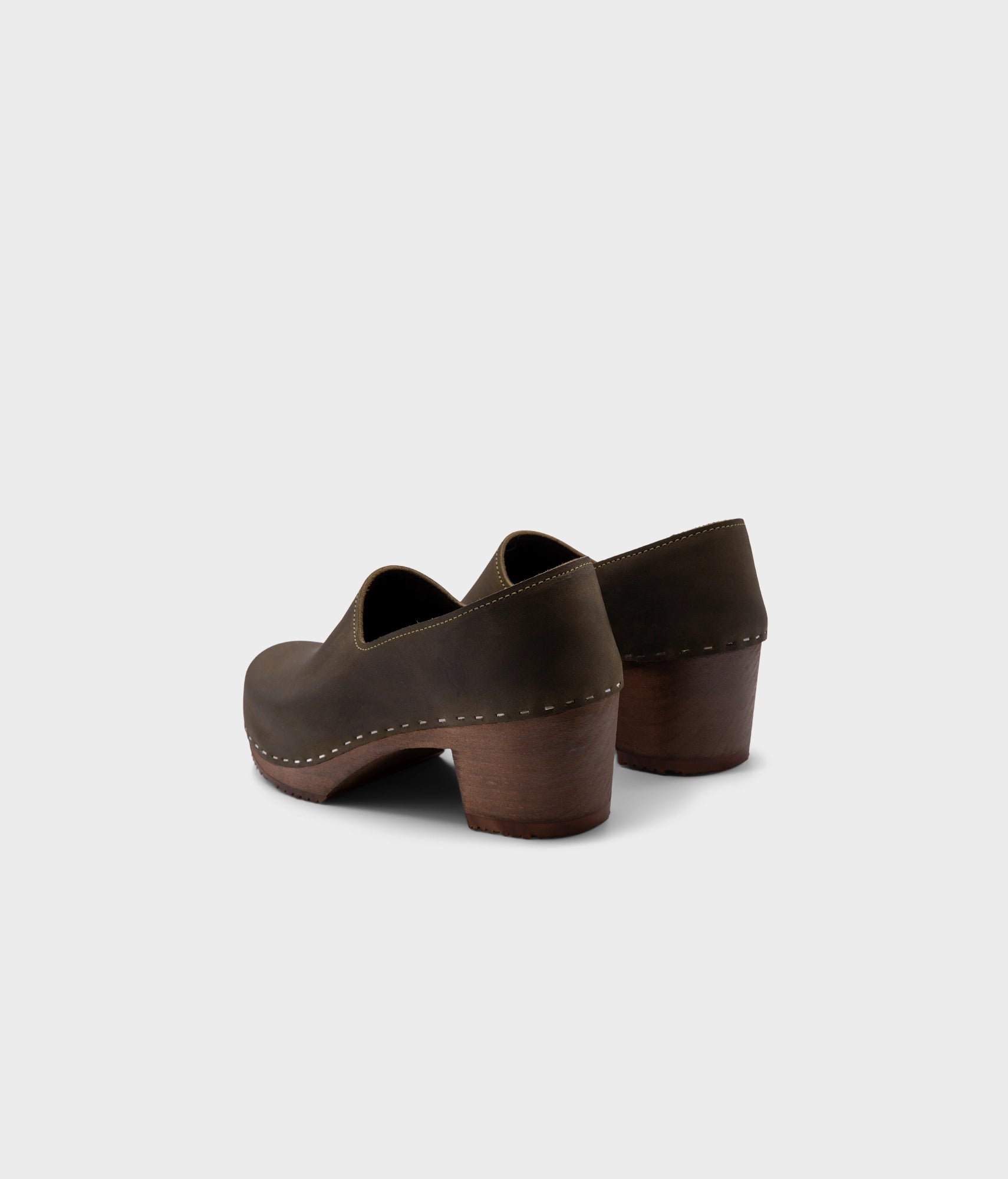 high heeled closed-back clogs in olive green nubuck leather stapled on a dark wooden base
