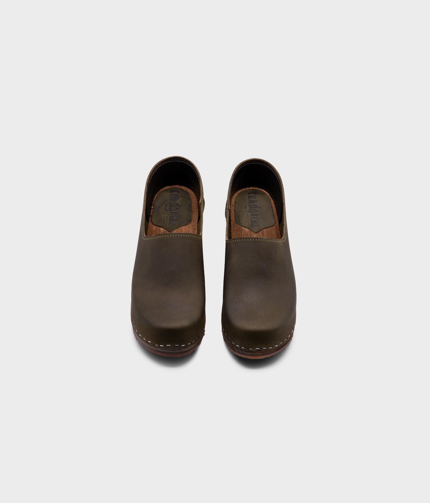 high heeled closed-back clogs in olive green nubuck leather stapled on a dark wooden base