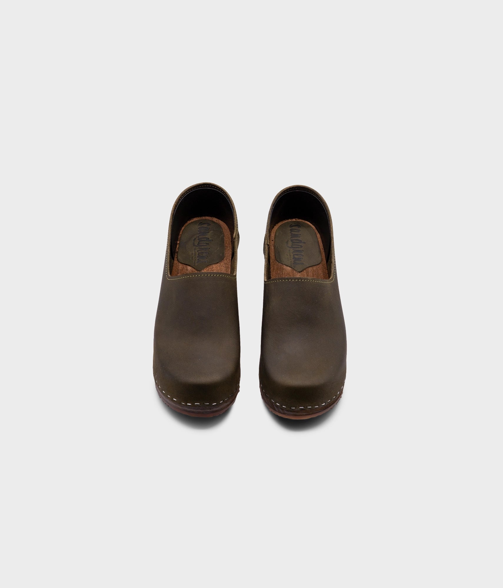 high heeled closed-back clogs in olive green nubuck leather stapled on a dark wooden base