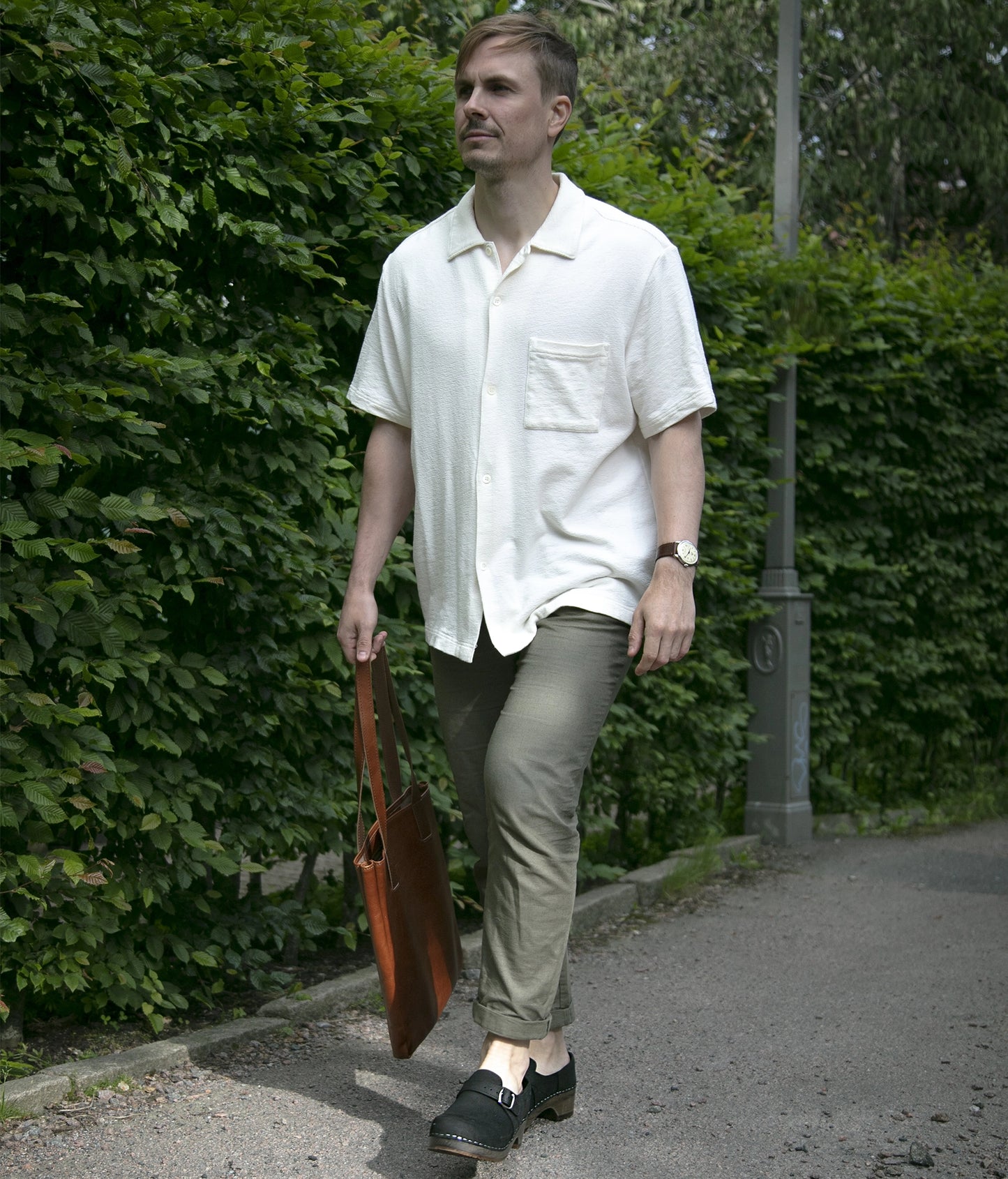 Man walking in closed-back clogs in black nubuck leather stapled on a dark wooden base with a silver buckle