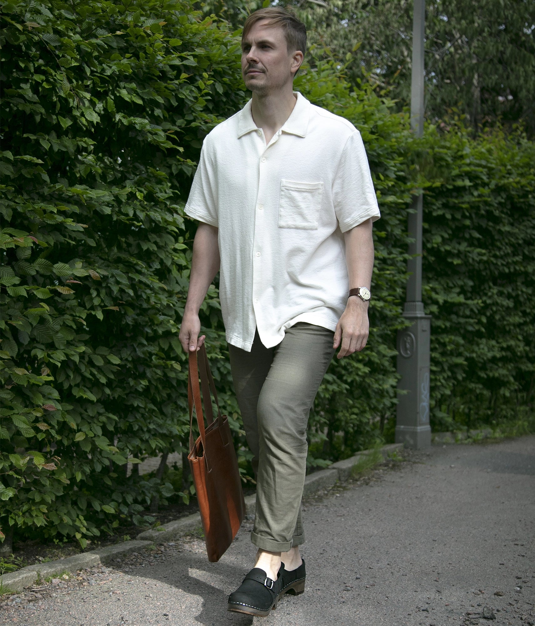 Man walking in closed-back clogs in black nubuck leather stapled on a dark wooden base with a silver buckle