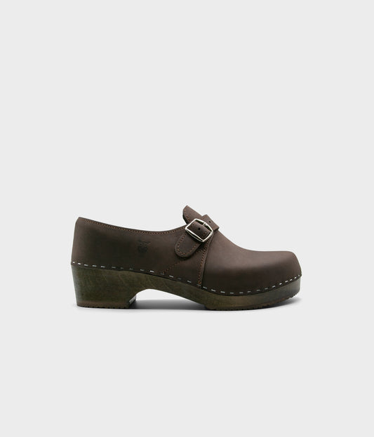 men's closed-back clogs in fudge brown nubuck leather stapled on a dark wooden base with a silver buckle