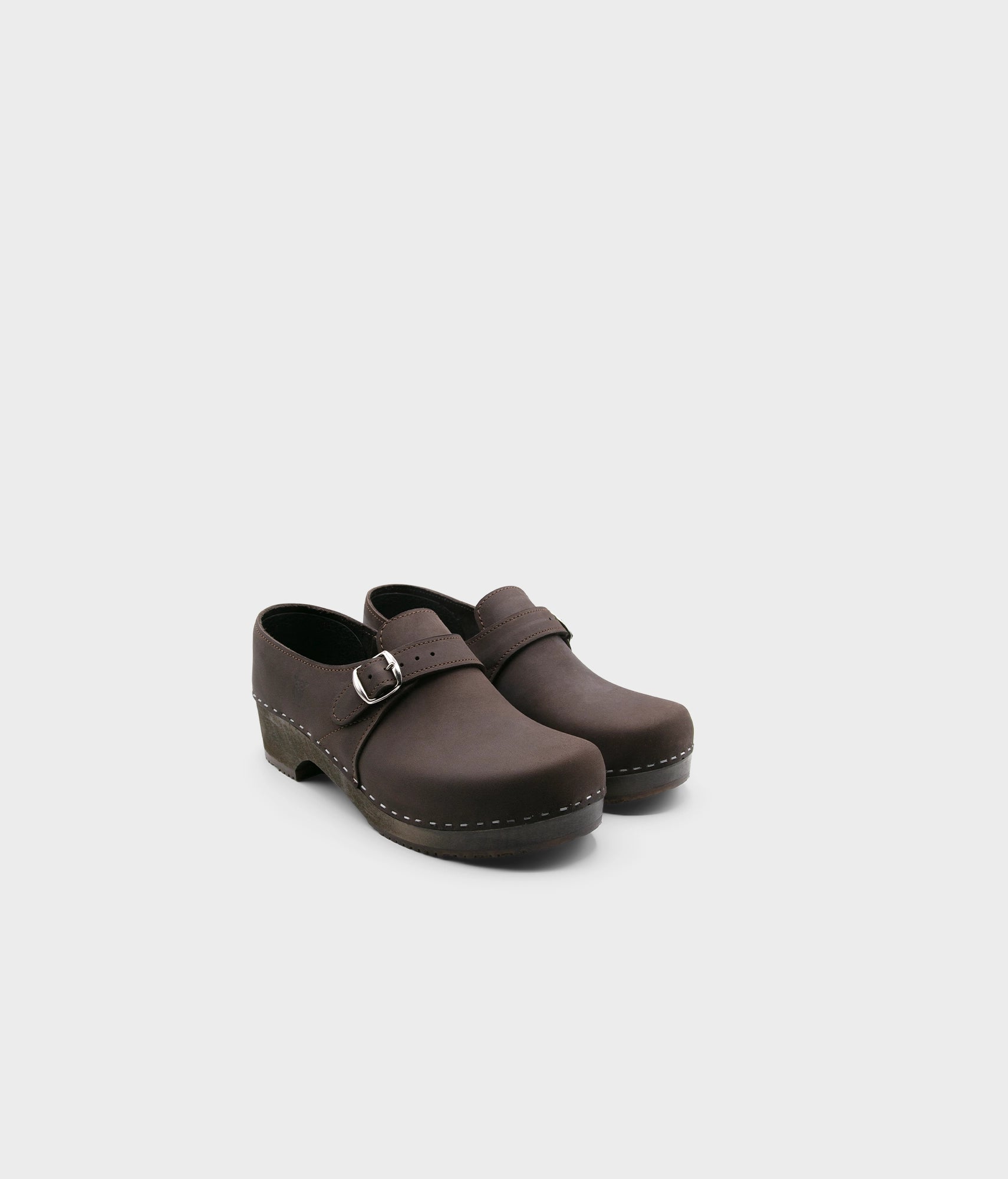 men's closed-back clogs in fudge brown nubuck leather stapled on a dark wooden base with a silver buckle