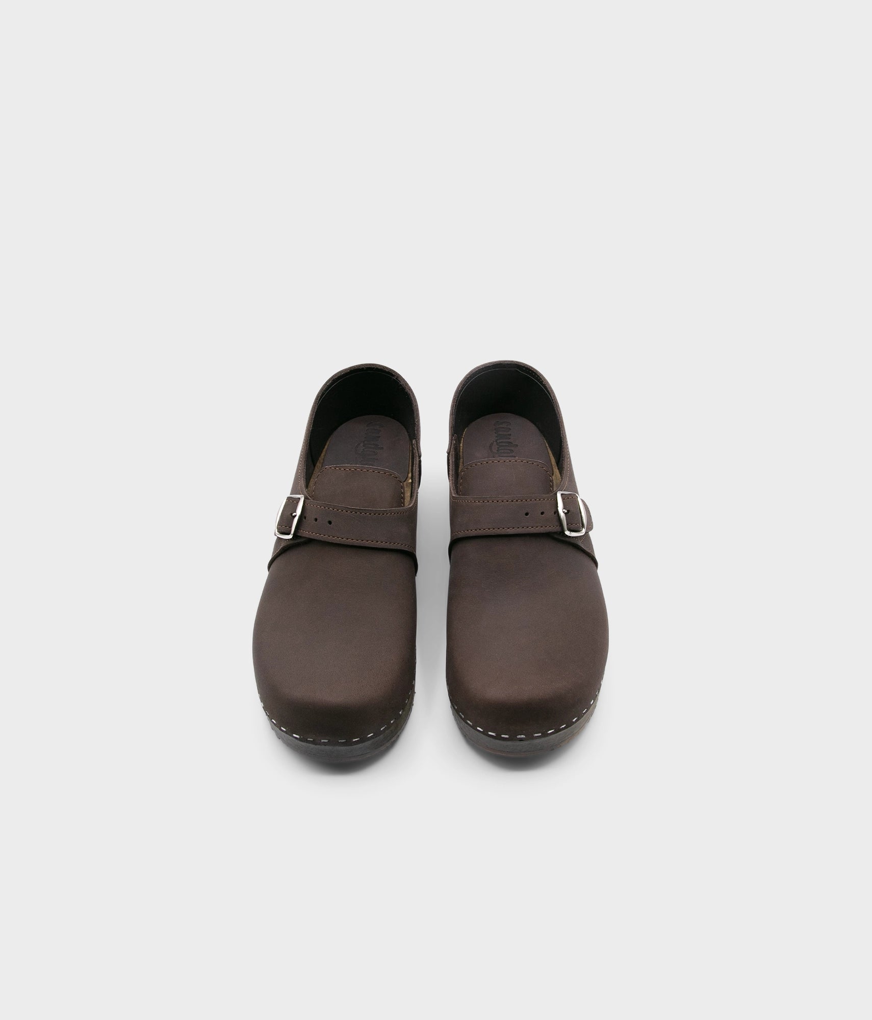 men's closed-back clogs in fudge brown nubuck leather stapled on a dark wooden base with a silver buckle