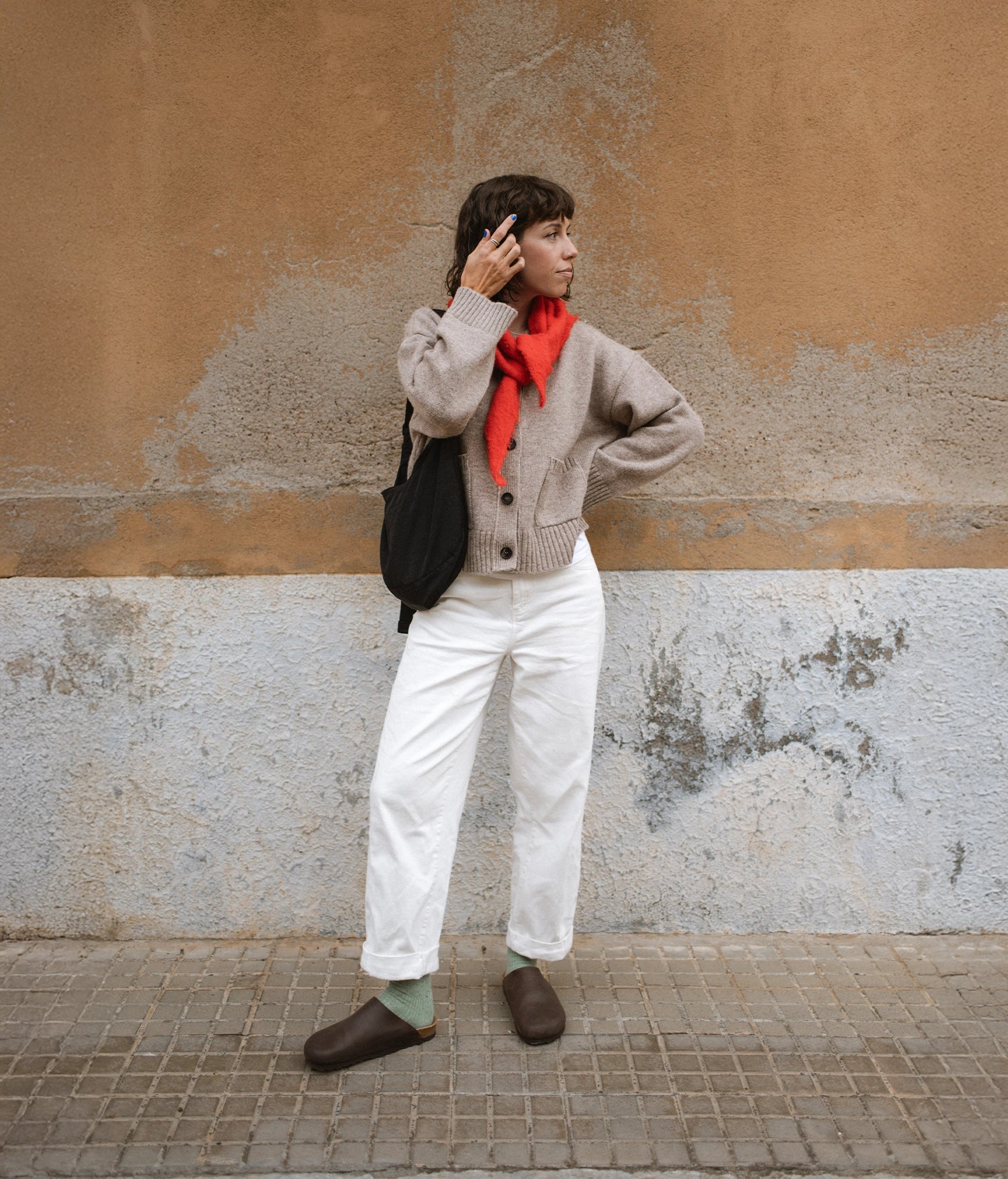 Person wearing a gray sweater, white pants, and brown cork sandals 
against a textured wall.